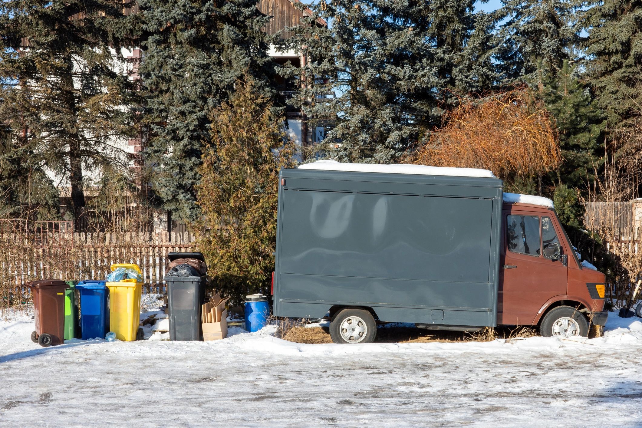 Service vehicle parked near waste bins in a snowy yard